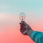 hand outstretched over a pink and blue gradient background holding a lightbulb.